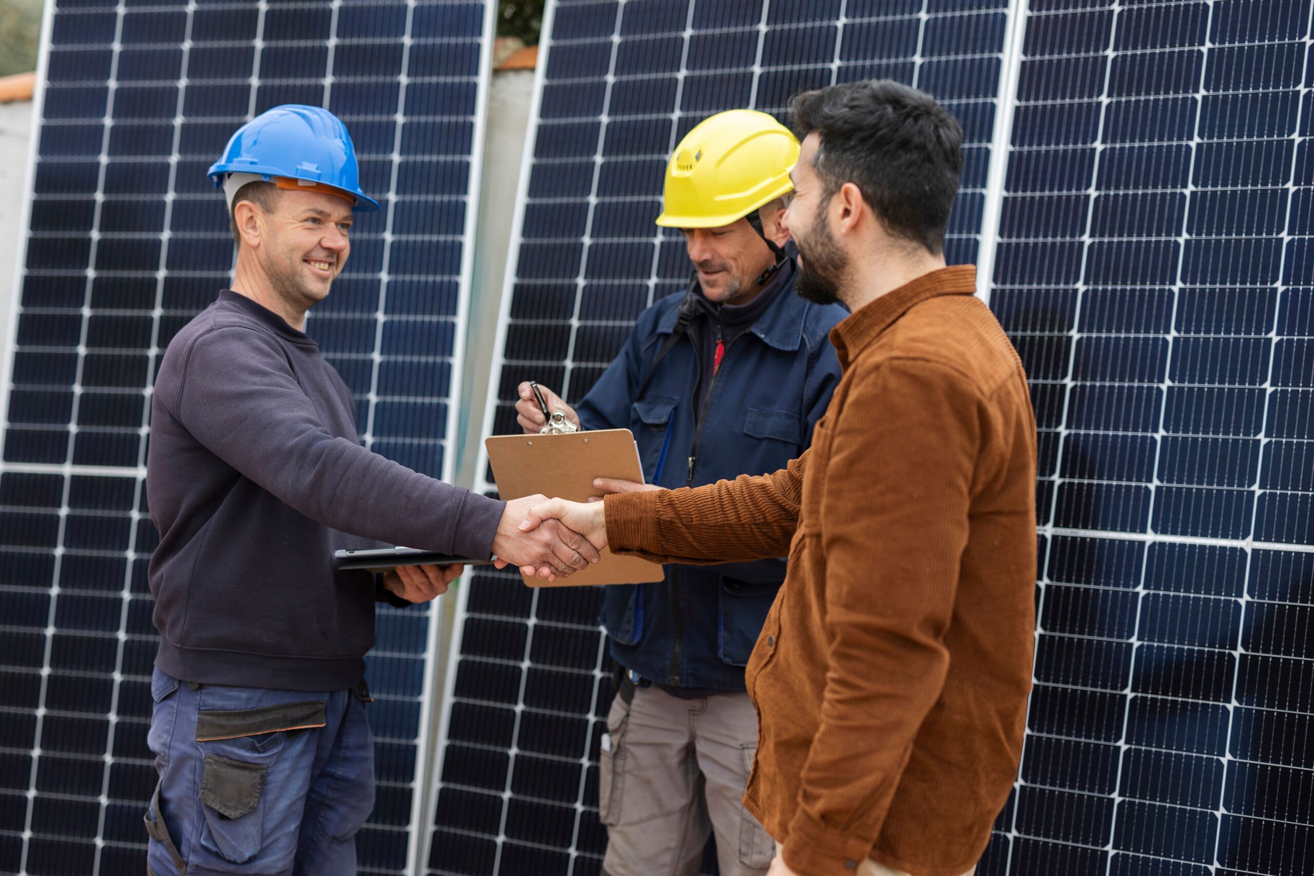 Drei Personen stehen vor einer Solaranlage. Zwei Personen geben sich die Hand 