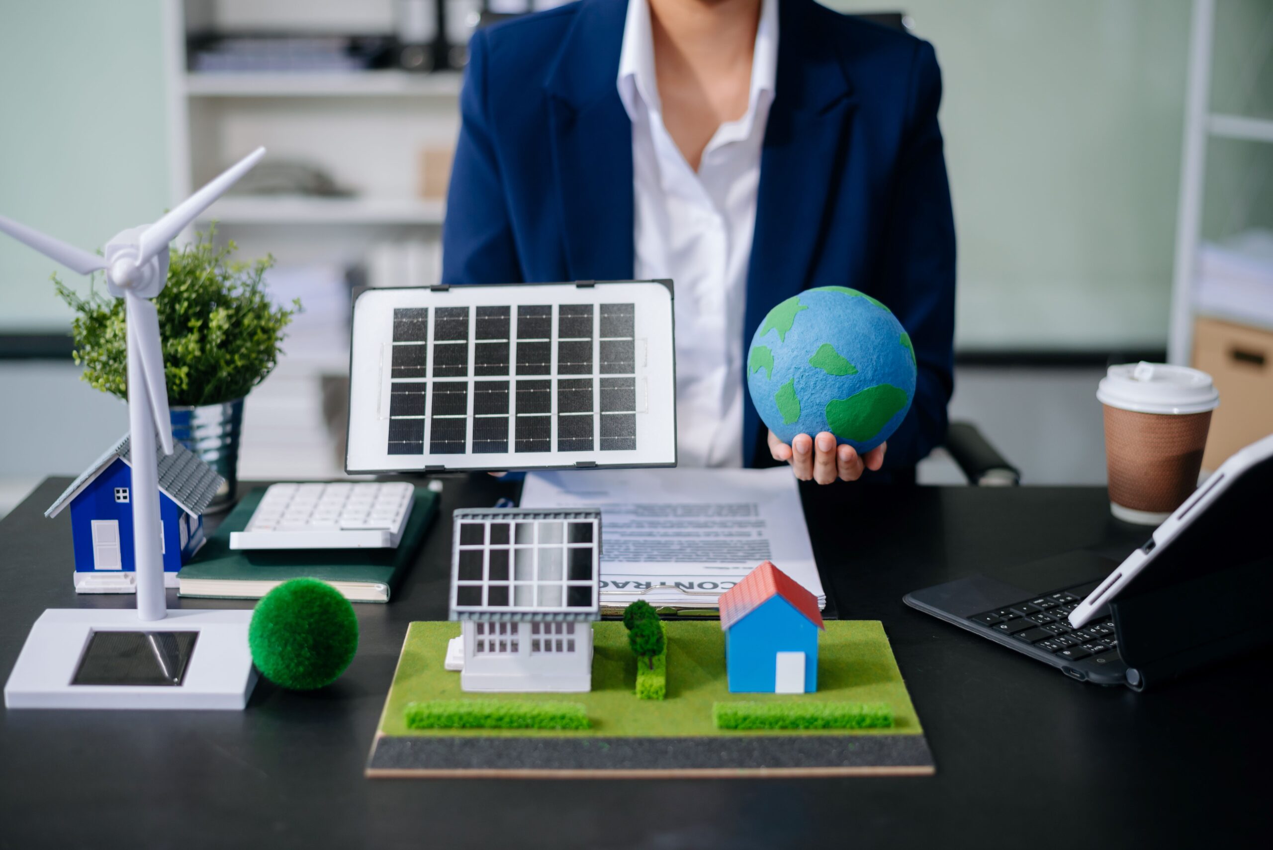 Eine Person hält eine Solaranlage über ein Miniatur Haus mit einer kleinen Weltkugel 